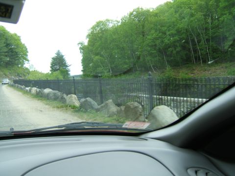 1998 Ford Taurus - A view from the driver's seat shows a road bordered by rocks and a fence, with trees in the background and another vehicle ahead.