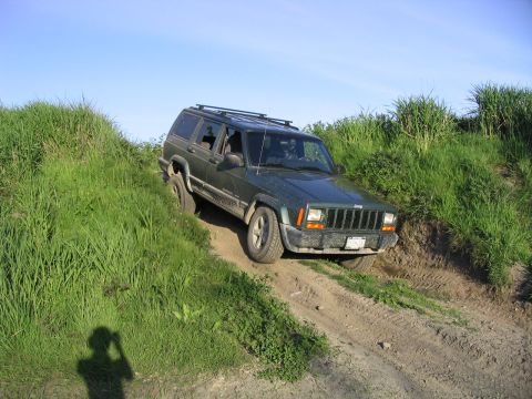 2000 Jeep Cherokee - A green 2000 Jeep Cherokee navigates a dirt trail with grassy hills on either side.