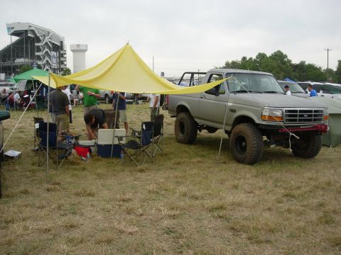 1995 Ford Bronco - A lifted Ford F-Series truck is parked near a campsite with a yellow canopy and chairs.