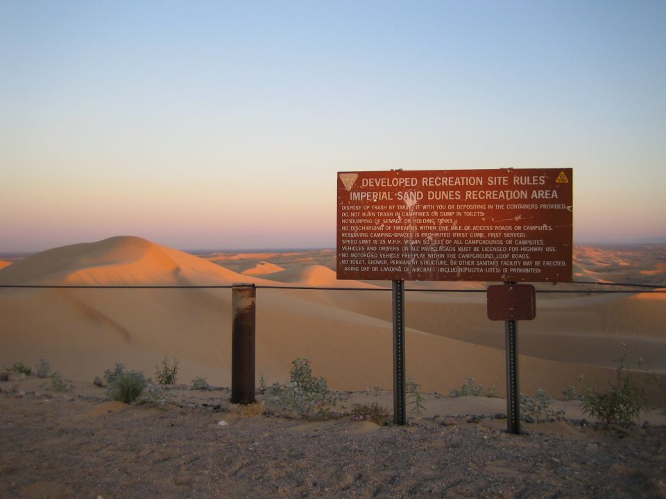 Sign with rules for Imperial Sand Dunes Recreation Area, with sand dunes in background at sunset