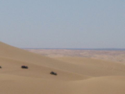 1968 Ford Mustang - Multiple vehicles are scattered across vast sand dunes, with a distant horizon under a pale blue sky.