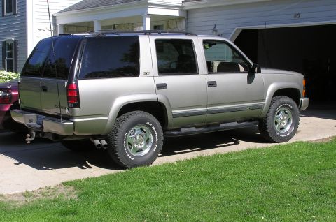 2000 Chevrolet Tahoe - A silver SUV is parked in front of a garage, with a portion of another vehicle visible to the left.