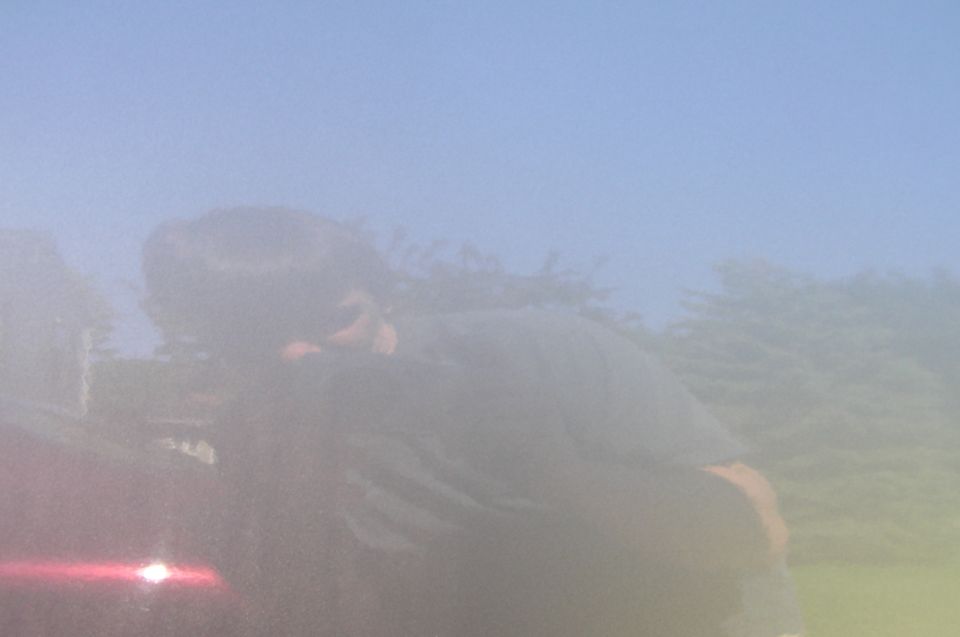 Reflection of a person wearing sunglasses and a dark shirt in the side door of a red vehicle