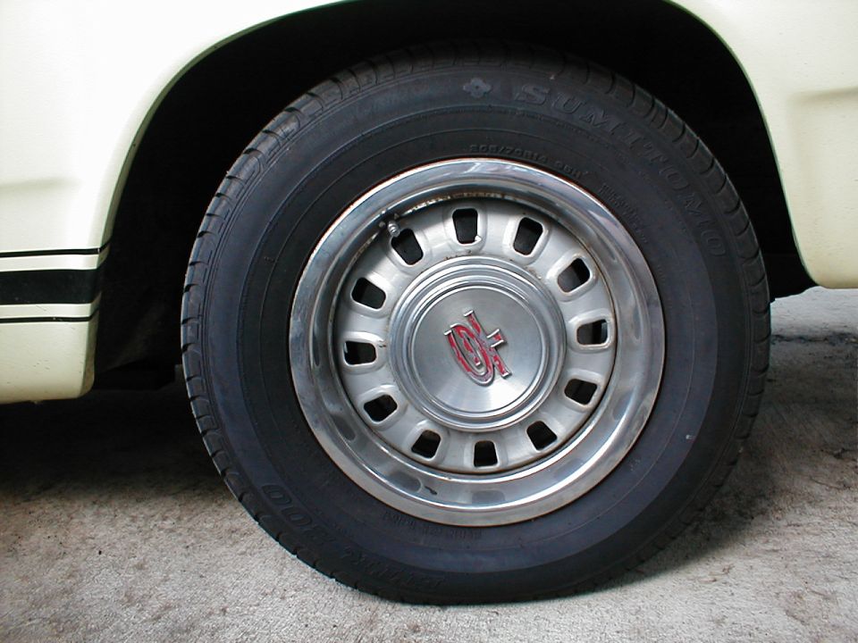 Close-up of chrome slotted hubcap with red emblem on Sumitomo tire of a cream classic car