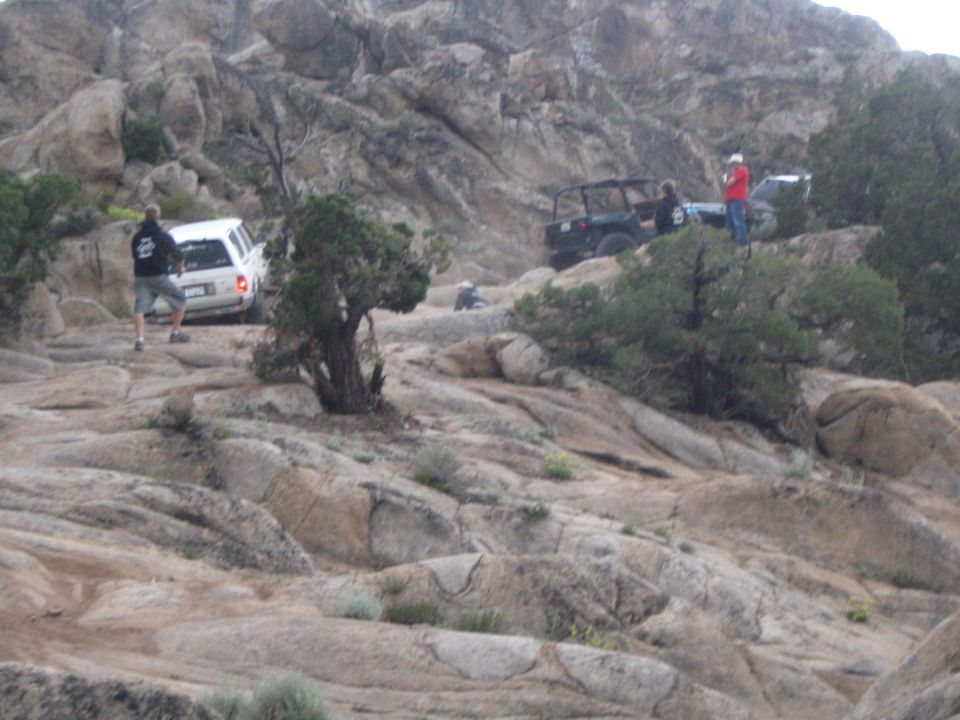 People and a white SUV plus a doorless 4x4 spread across a vast slickrock area