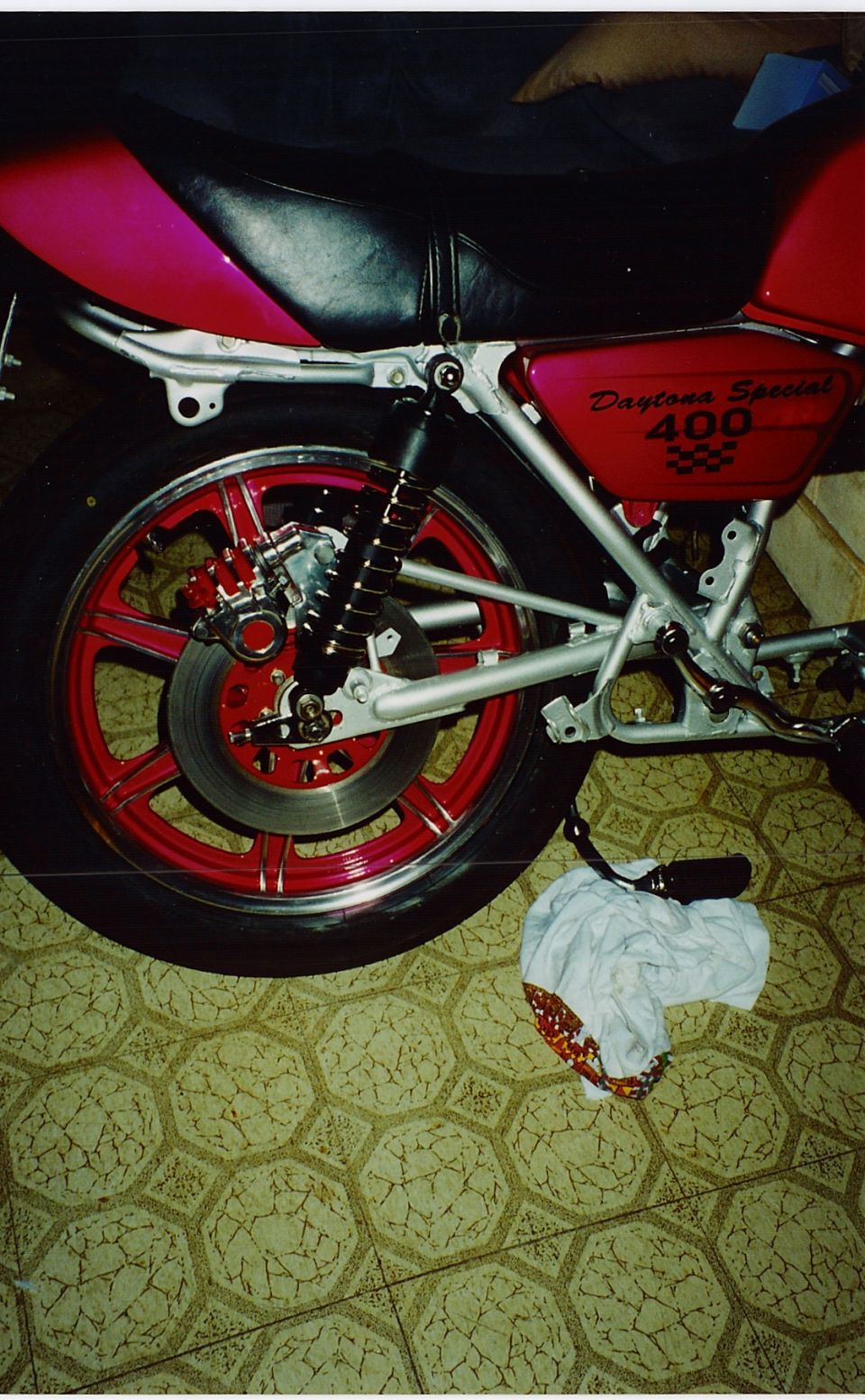 Rear wheel and swingarm of a red Yamaha Daytona Special 400 with red mag wheel on tile floor