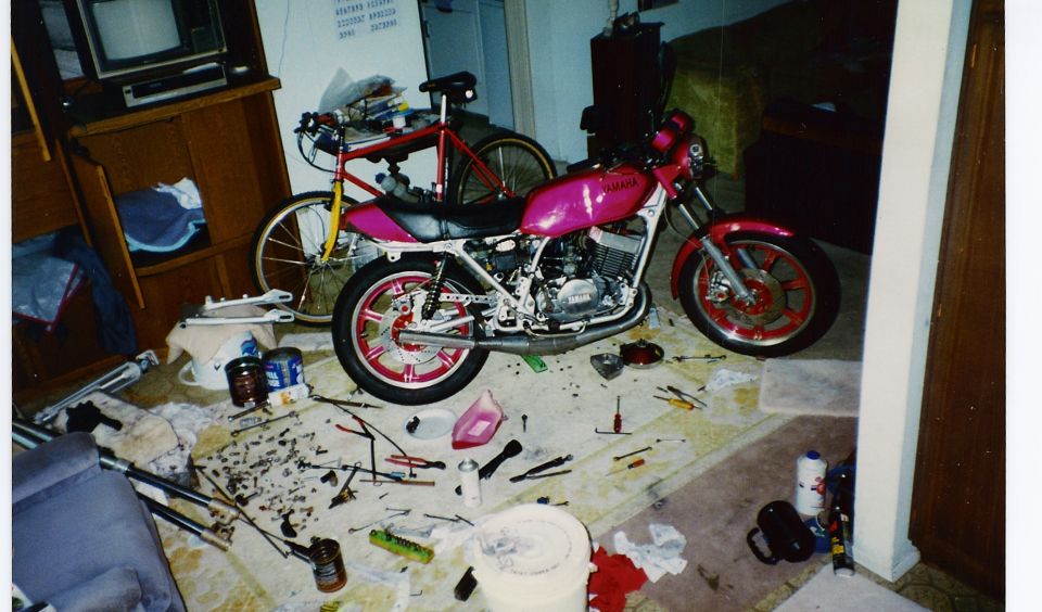 Pink Yamaha motorcycle inside a room surrounded by scattered tools and parts during a rebuild