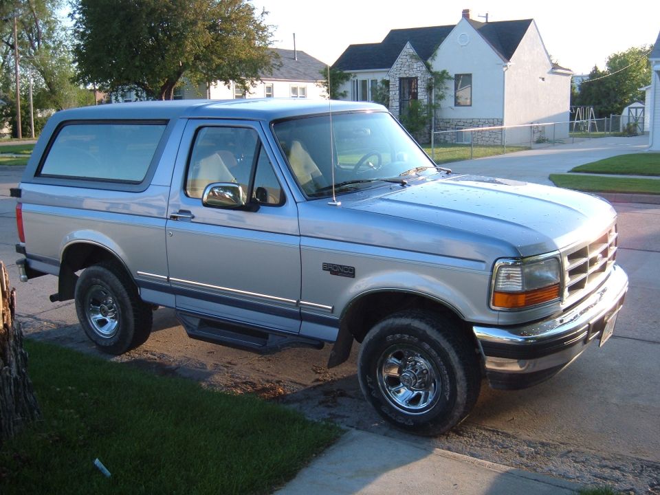 Two-tone blue and silver 1996 Ford Bronco with chrome wheels and running boards parked on a residential street