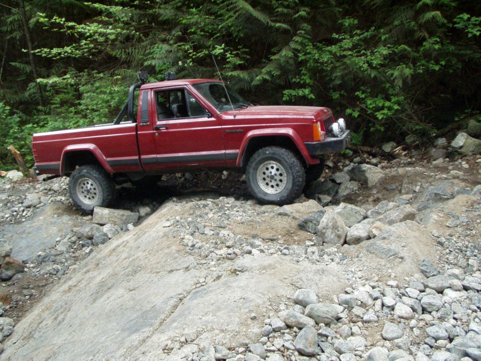 Red Jeep Comanche pickup truck navigating a rocky off-road trail