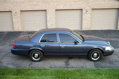 1998 Ford Crown Victoria - A dark blue 1998 Ford Crown Victoria is shown from the side, parked on a concrete driveway in front of a brick building.