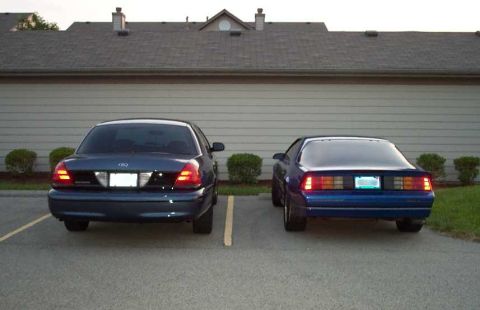1998 Ford Crown Victoria - Two cars, a Ford Crown Victoria and a Chevrolet Camaro, are parked in front of a building.
