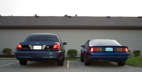 1998 Ford Crown Victoria - Two cars, a Ford and a Chevrolet, are parked side-by-side in front of a garage door.