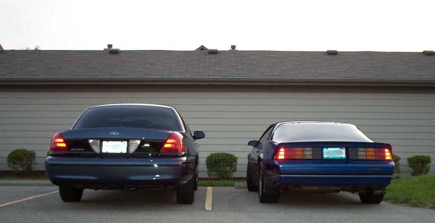 Two dark blue cars, a sedan and a coupe, parked rear-facing near a building.