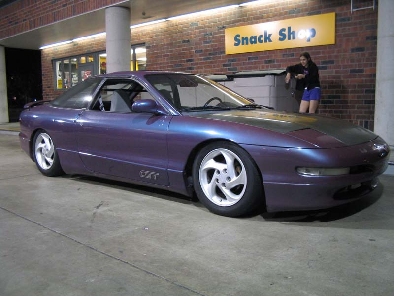 Purple Ford Probe GT coupe with carbon hood parked at night outside a Snack Shop