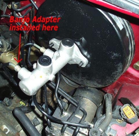 1995 Ford Probe - Close-up of a brake master cylinder and booster assembly with an arrow pointing to where a banjo adapter is installed.