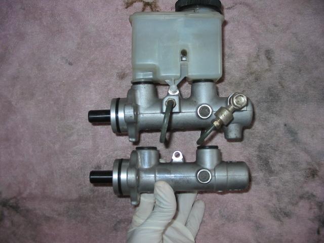 Two brake master cylinders, one with a reservoir, are shown. A gloved hand holds the bottom one