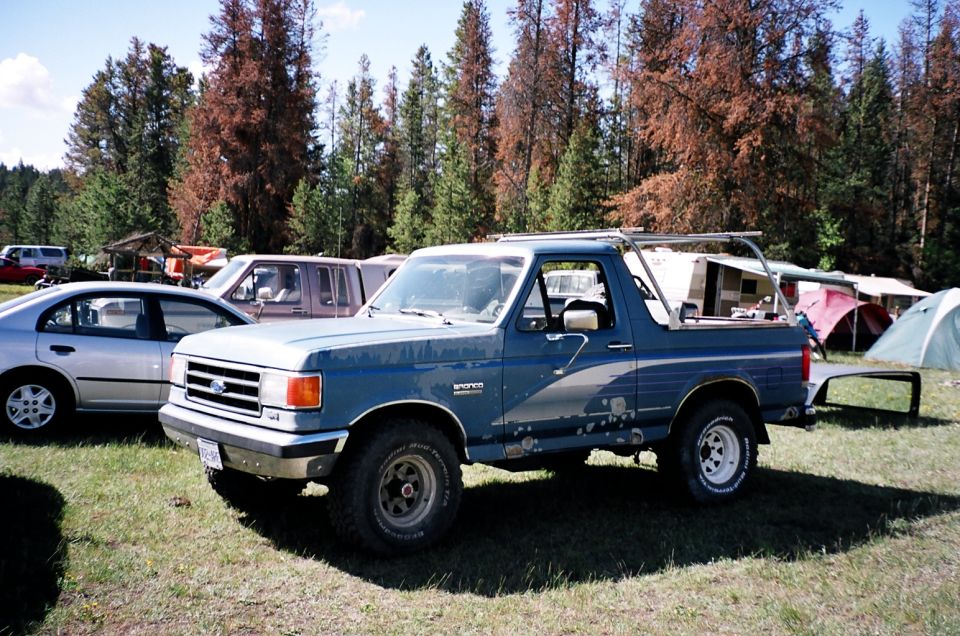 Blue Ford Bronco full-size SUV parked on grass at a campground next to a silver sedan