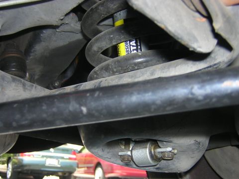 1992 Ford Crown Victoria - Close-up of a car's rear suspension system, showing a shock absorber and coil spring, with other vehicles blurred in the background.