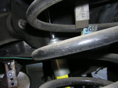 1992 Ford Crown Victoria - Tight close-up of a rear coil spring with a shock absorber running down through its center, photographed from underneath on a light-colored…