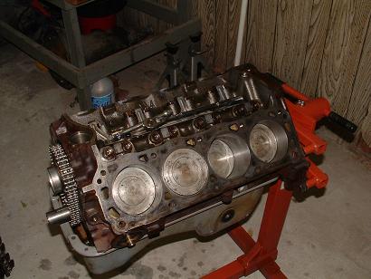 1985 Ford LTD Crown Victoria - Engine block on an orange stand, displaying cylinders and a timing chain, with garage shelving in the background.