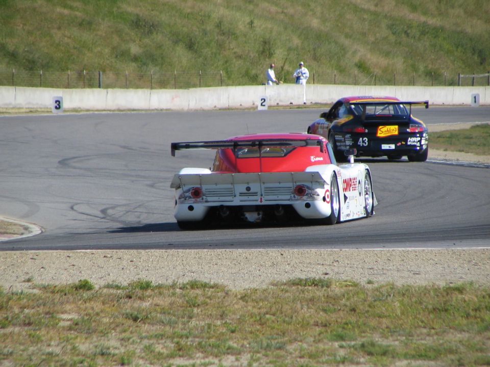 Two race cars on a track, one white and red with a large rear wing, the other black with a smaller wing and number 43