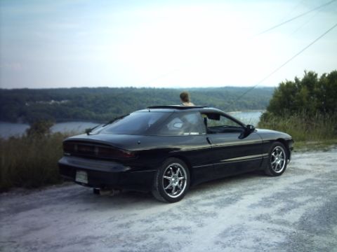 1995 Ford Probe - A black 1995 Ford Probe is parked on a dirt road with a scenic view of water and trees.