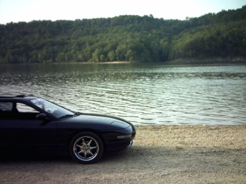 1995 Ford Probe - A black 1995 Ford Probe sits by the water on a sunny day, with a forested hill behind it.