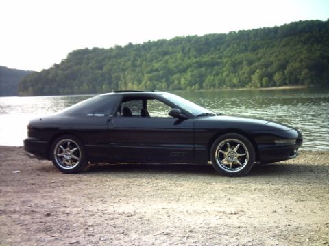 1995 Ford Probe - A black Ford Probe GT sits by the water's edge on a sunny day.