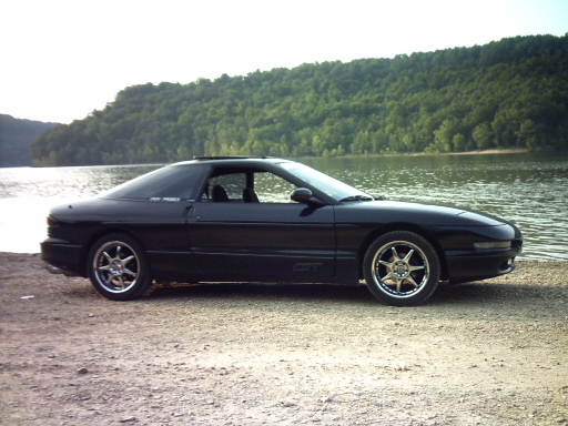 Black Ford Probe GT parked on gravel by a lake, side view