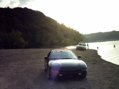 1995 Ford Probe - A dark coupe sits by the water's edge as the sun sets behind a tree-covered hill.