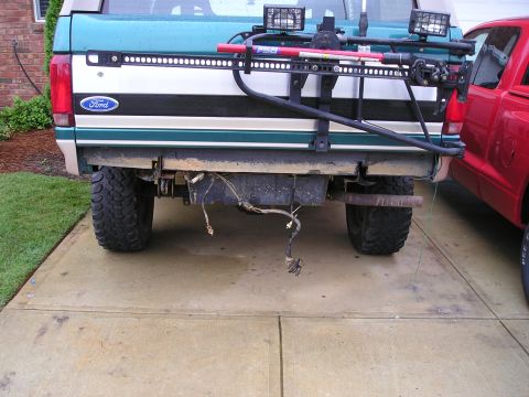 1996 Ford Bronco - Rear view of a 1996 Ford Bronco showing its custom bumper and spare tire carrier, with a red truck nearby.