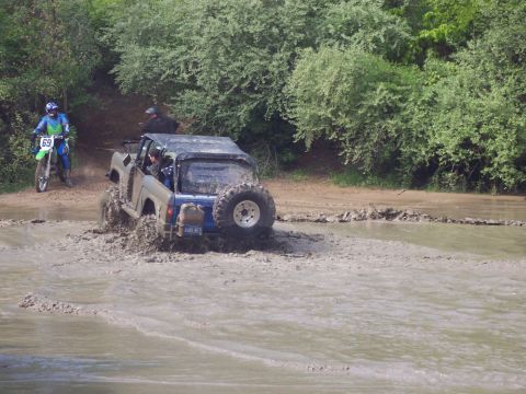 1974 Ford Bronco - A dirt bike and an off-road vehicle navigate a muddy trail with trees in the background.