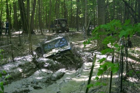 1974 Ford Bronco - Two off-road vehicles navigate a challenging muddy trail in a forest environment.