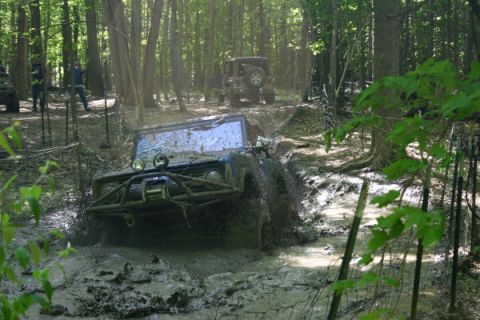 1974 Ford Bronco - A blue 1974 Ford Bronco struggles through deep mud on an off-road trail, with another vehicle visible in the background.