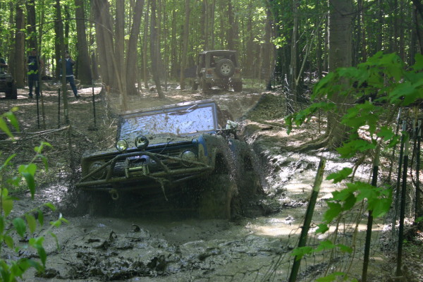 Front view of a blue 1974 Ford Bronco navigating a muddy off-road course