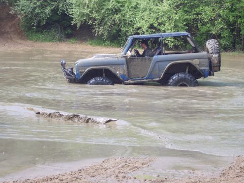 1974 Ford Bronco - A driver navigates a blue Ford Bronco through a shallow, muddy body of water.