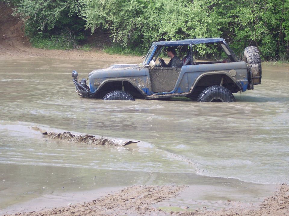 Blue Ford Bronco driving through muddy water, tires submerged