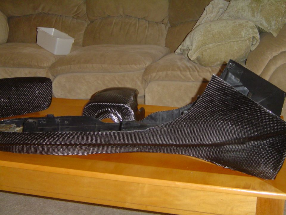 Carbon fiber car interior trim pieces on a table, with a couch in the background