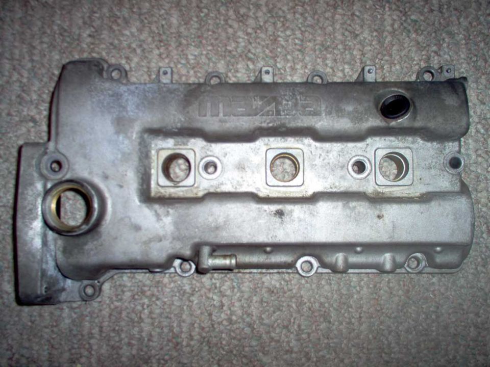 Aluminum Mazda-branded engine valve cover with spark plug tube holes on carpet