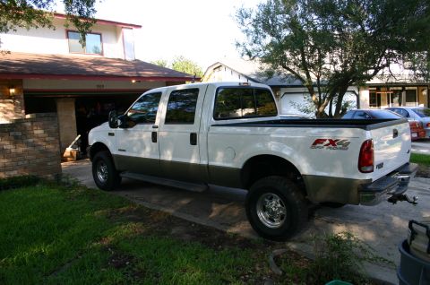 2004 Ford F-350 - A white and brown 2004 Ford F-350 pickup truck is parked in a driveway next to a house.