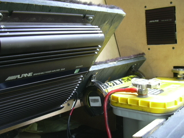 Alpine bridgeable amplifier on angled rack next to yellow-lid battery box with red cable