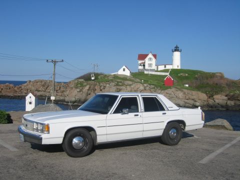 1991 Ford LTD Crown Victoria - A white sedan is parked near a lighthouse on a sunny day.