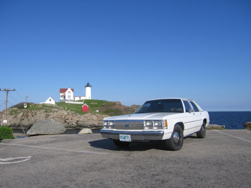 White Ford Crown Victoria sedan parked at ocean overlook with lighthouse behind