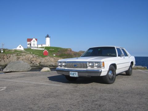 1991 Ford LTD Crown Victoria - A white Ford sedan is parked near a lighthouse with the ocean in the background.