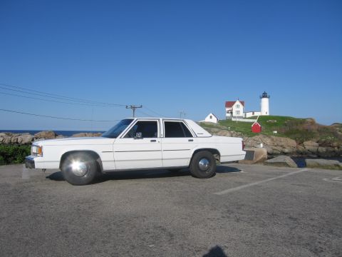1991 Ford LTD Crown Victoria - A white sedan is parked near a lighthouse on a sunny day.