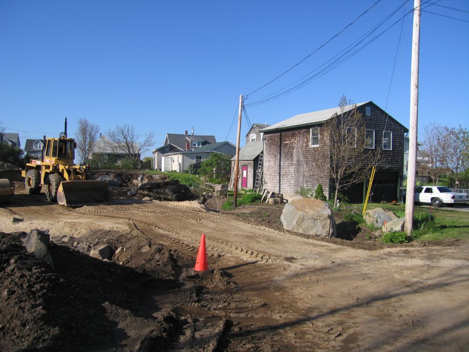 Yellow front loader on a construction site with a white sedan in the background