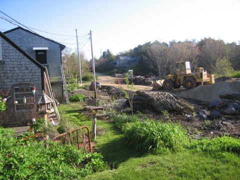 1991 Ford LTD Crown Victoria - A construction site features a yellow wheel loader parked on a mound of dirt, with a residential building and trees visible.
