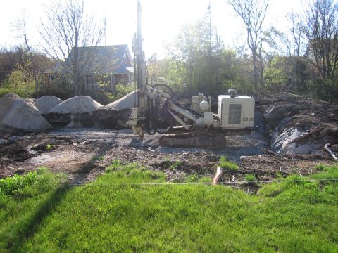 1991 Ford LTD Crown Victoria - A drilling rig is positioned at a construction site, with piles of sand and a house visible in the distance.