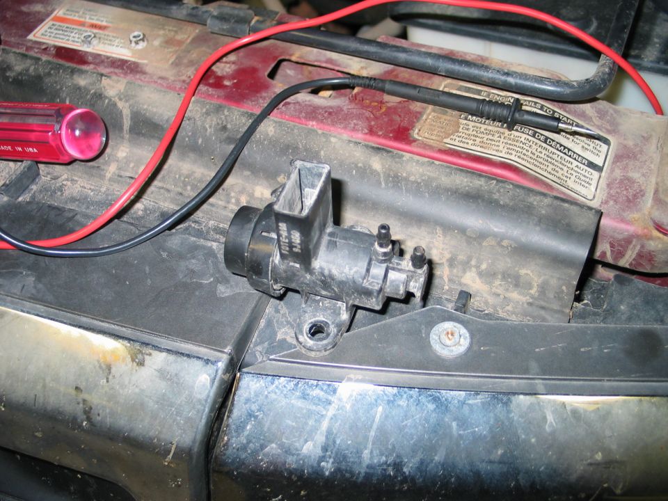 Black engine part with red and black wires connected, next to a red screwdriver