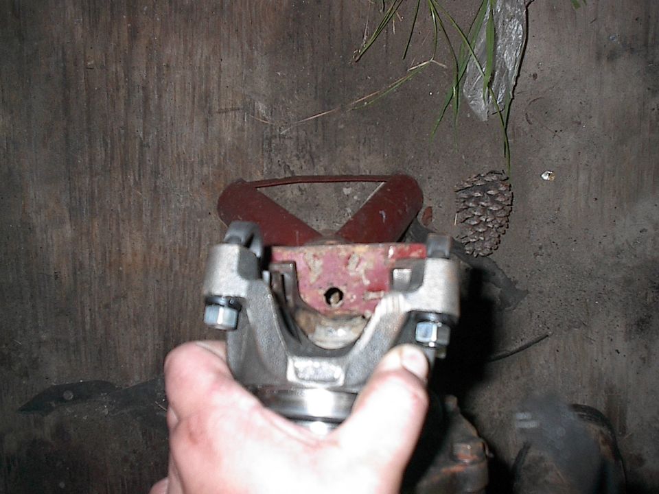 Driveshaft U-joint held by hand, red metal support in background